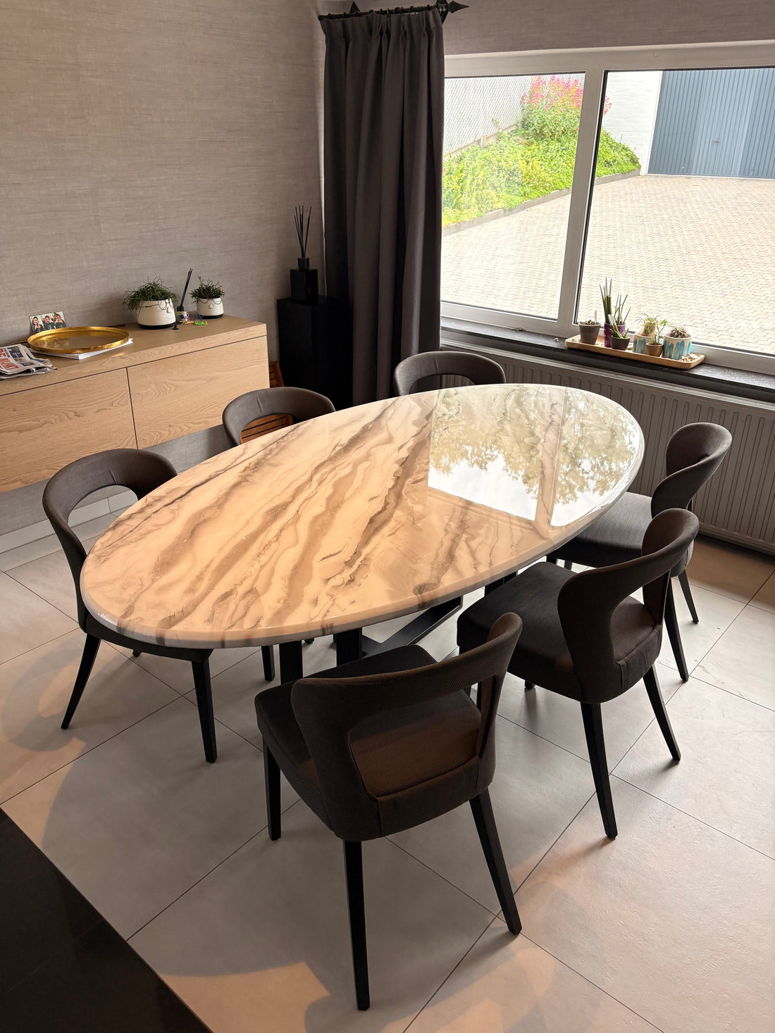 Custom oval epoxy resin dining table with warm sand and marble effect finish on black steel legs, installed in a client’s home — bespoke made-to-order furniture by Leonardo Gravina, Belgium