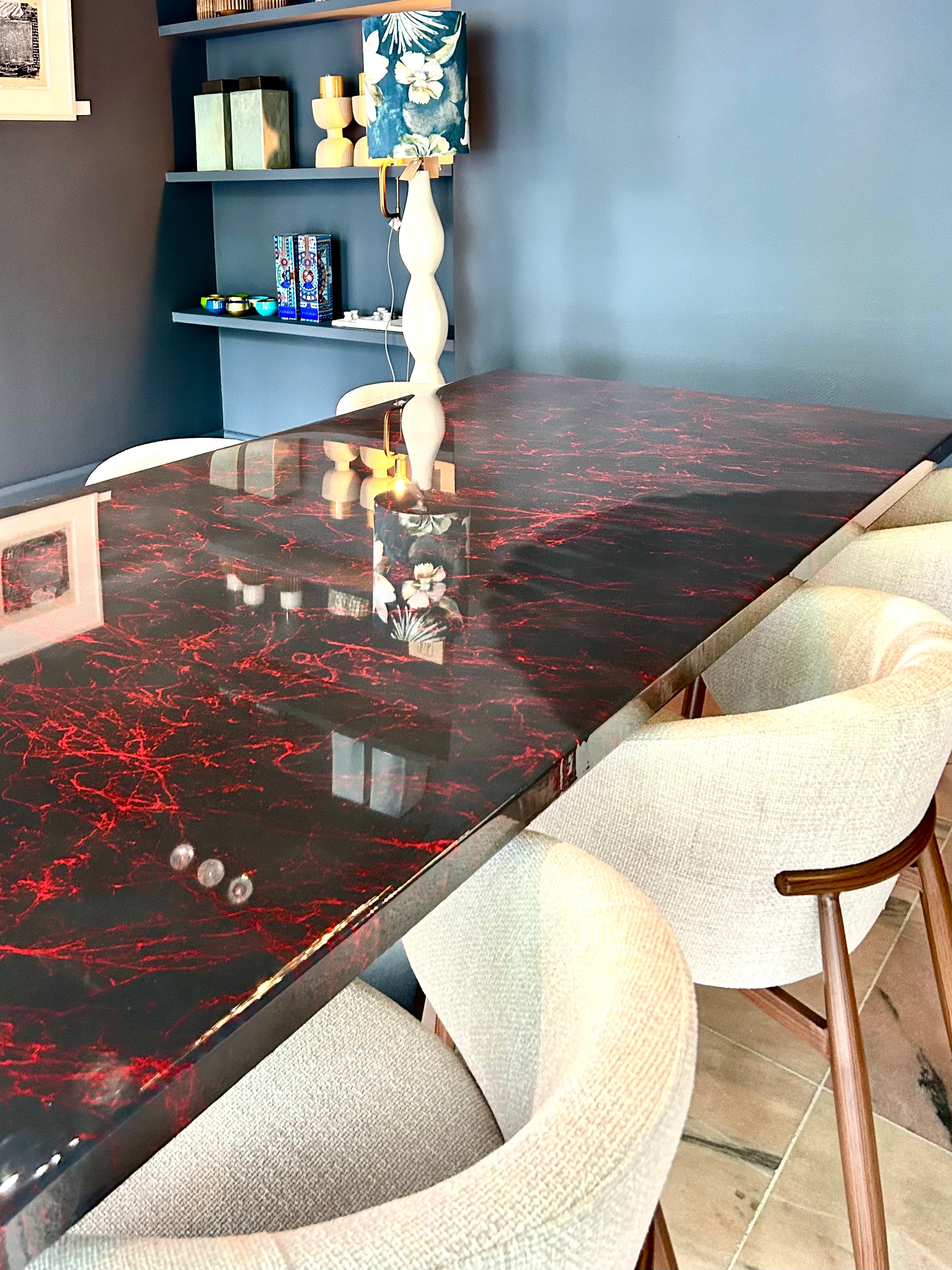 Rechthoekige donker grijze eettafel met rode marmerpatronen, omringd door beige stoelen.