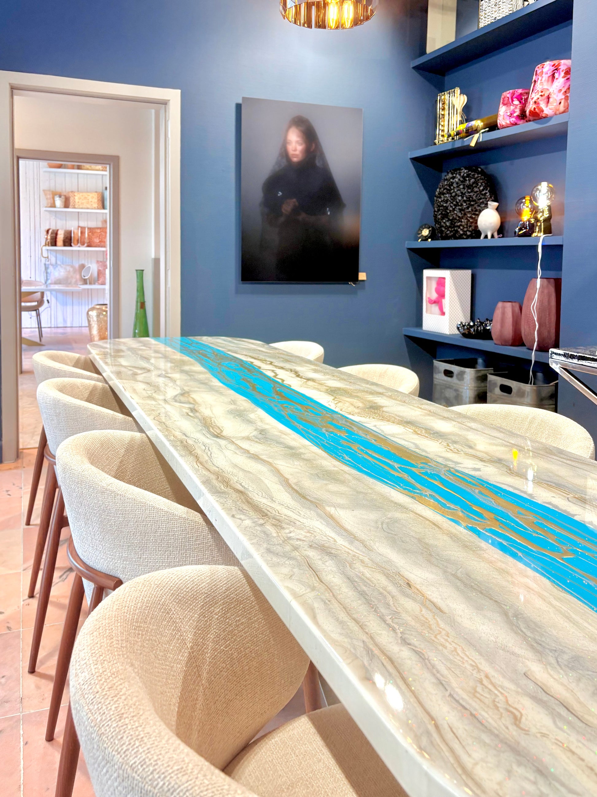 Lange eettafel met goud en zilver-marmerlook en turquoise rivier, omringd door beige stoelen.