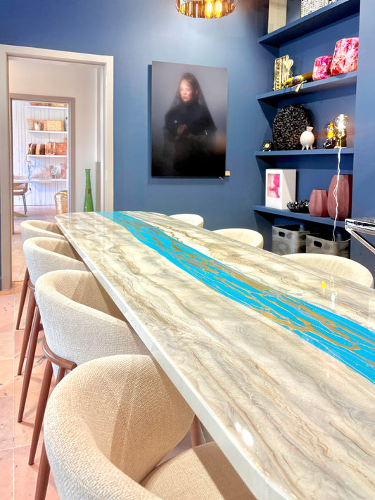 Lange eettafel met goud en zilver-marmerlook en turquoise rivier, omringd door beige stoelen.