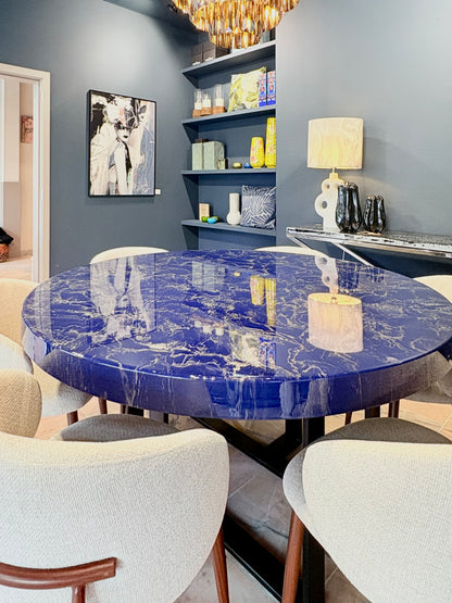 Ronde blauwe eettafel met zilver marmerlook, omringd door beige stoelen.