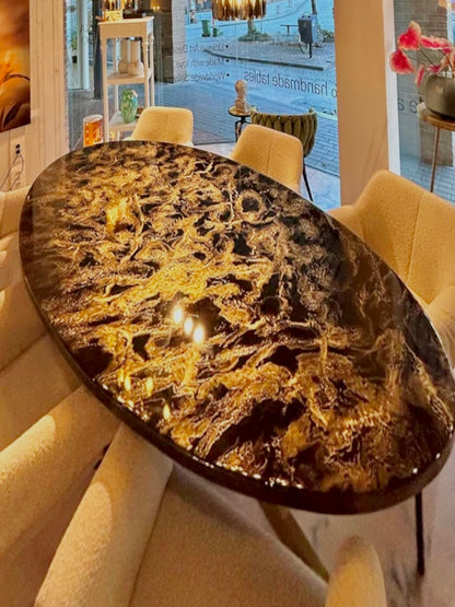 Ovale eettafel met een hoogglanzend zwart blad met goud-marmer patronen. De tafel staat in een moderne showroom met beige gestoffeerde stoelen eromheen. Op de achtergrond zijn grote ramen, kunstwerken en decoratieve objecten zichtbaar.