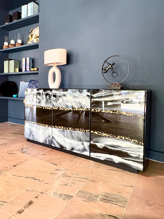 Zwart dressoir met marmerlook en gouden accenten tegen blauwe wand.