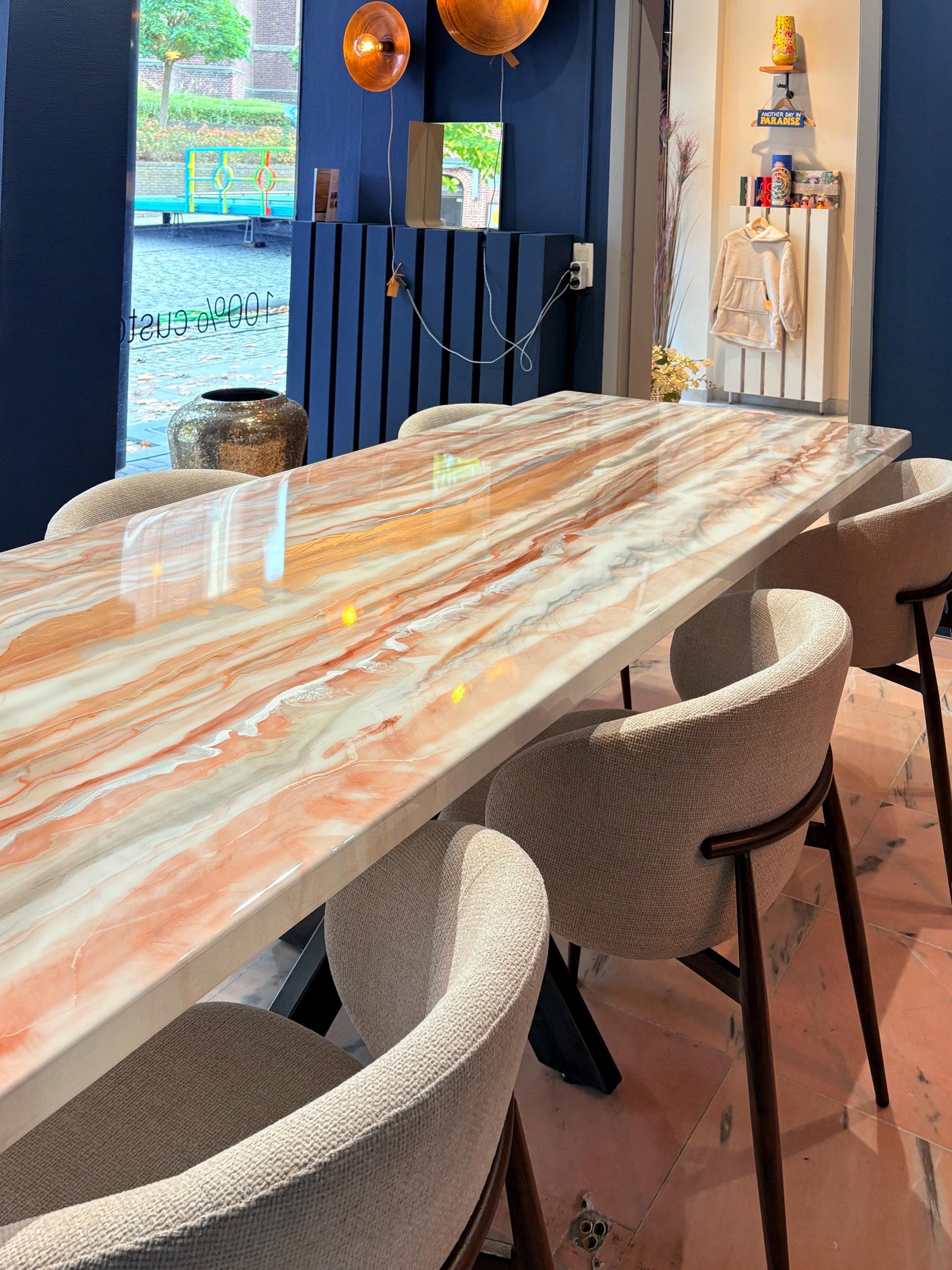 Rechthoekige eettafel met roos goud, koper, zilver en brons marmerlook, omringd door beige stoelen.